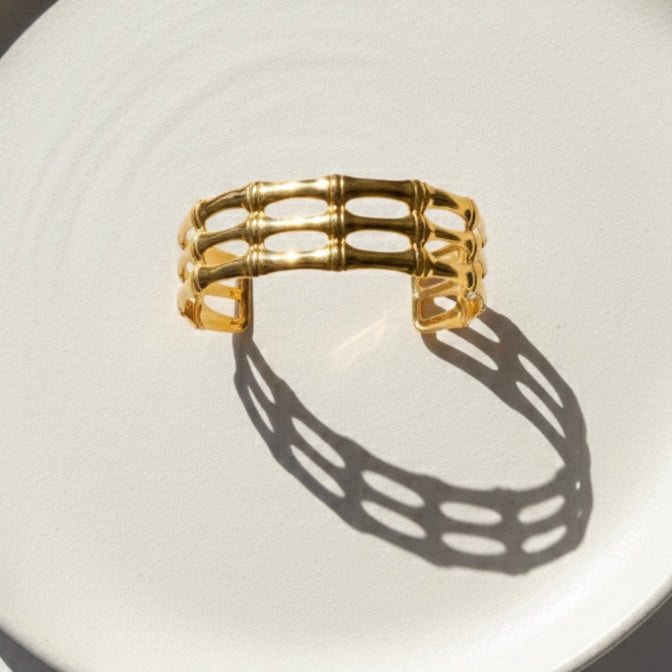 Wide gold cuff bracelet with openwork bamboo design on white background.