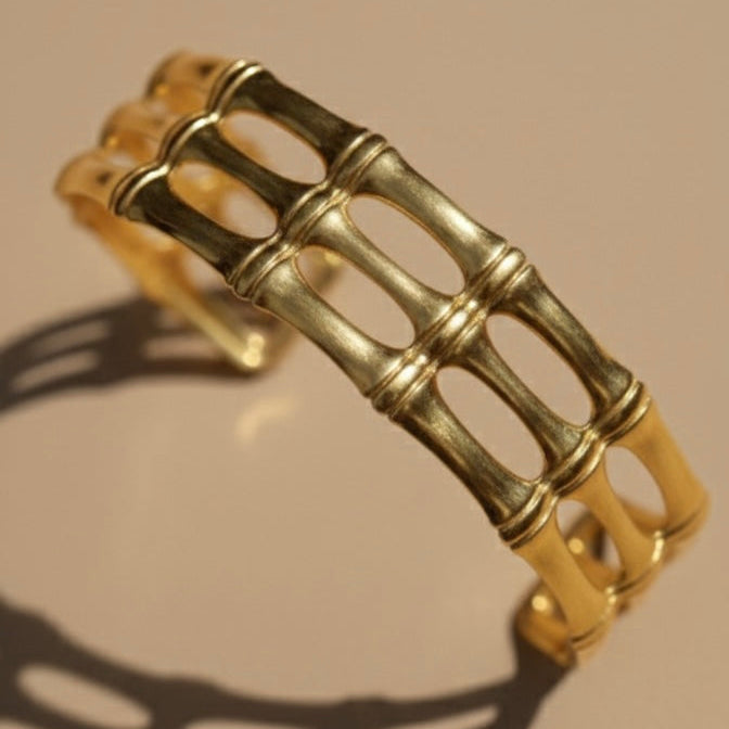 Wide gold cuff bracelet with openwork bamboo design on white background.