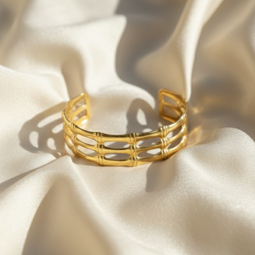 Wide gold cuff bracelet with openwork bamboo design on white background.