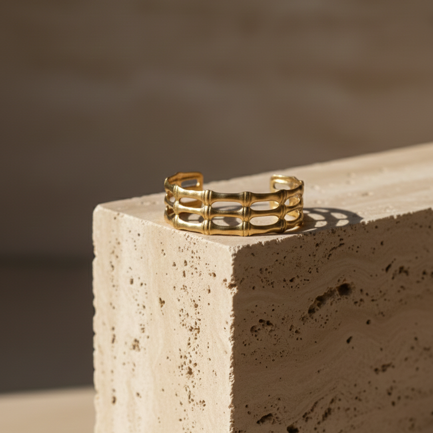 Wide gold cuff bracelet with openwork bamboo design on white background.