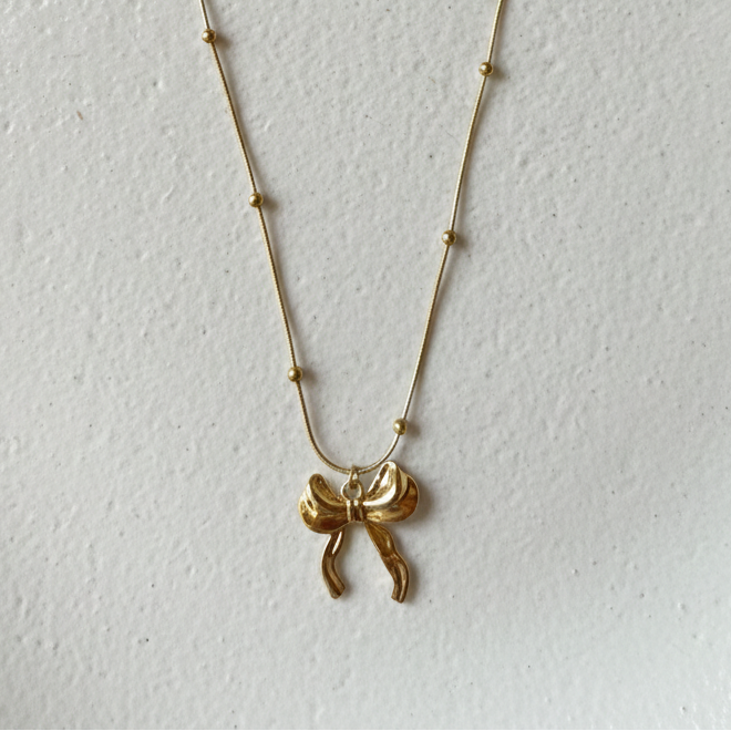 Gold 3D puffed bow necklace pendant on snake chain waterproof jewelry white background.