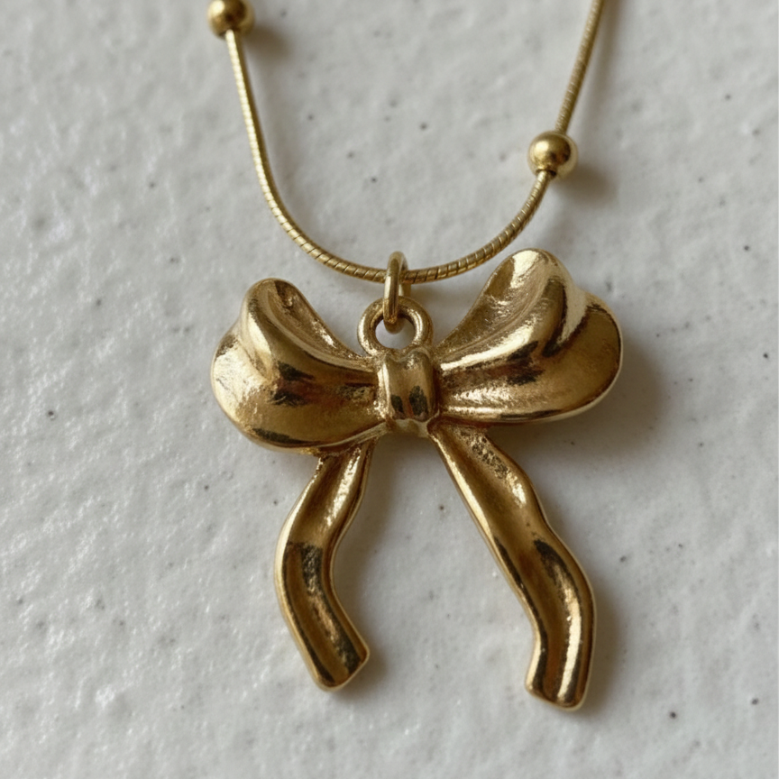 Gold 3D puffed bow necklace pendant on snake chain waterproof jewelry white background.