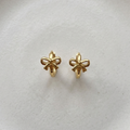 Gold ribbon bow huggie earrings on white ceramic plate.