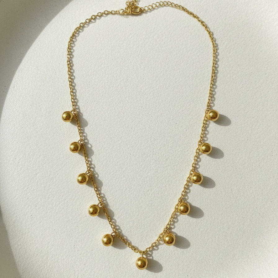Gold necklace with dangling gold ball charms in wooden jewelry box display.