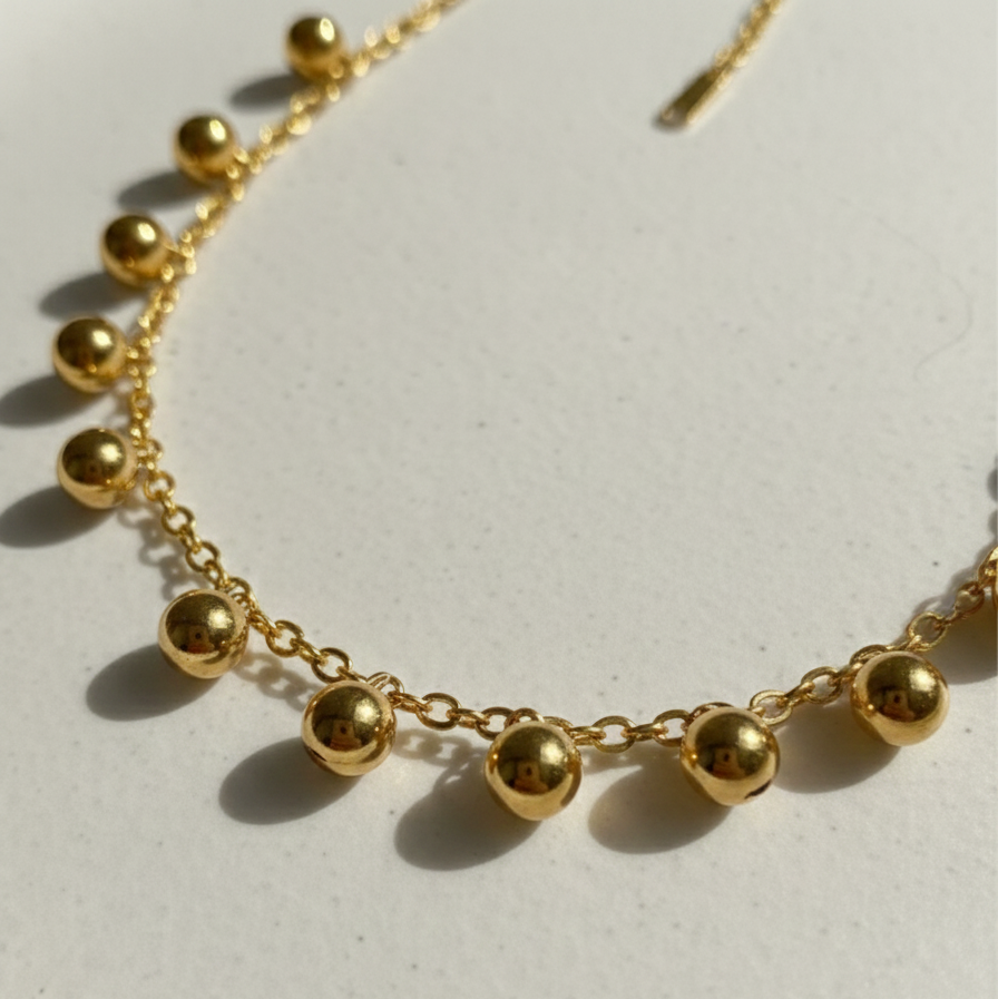 Gold necklace with dangling gold ball charms in wooden jewelry box display.
