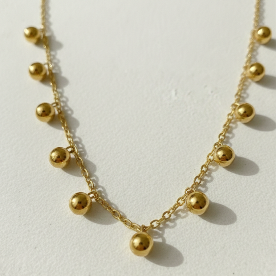 Gold necklace with dangling gold ball charms in wooden jewelry box display.