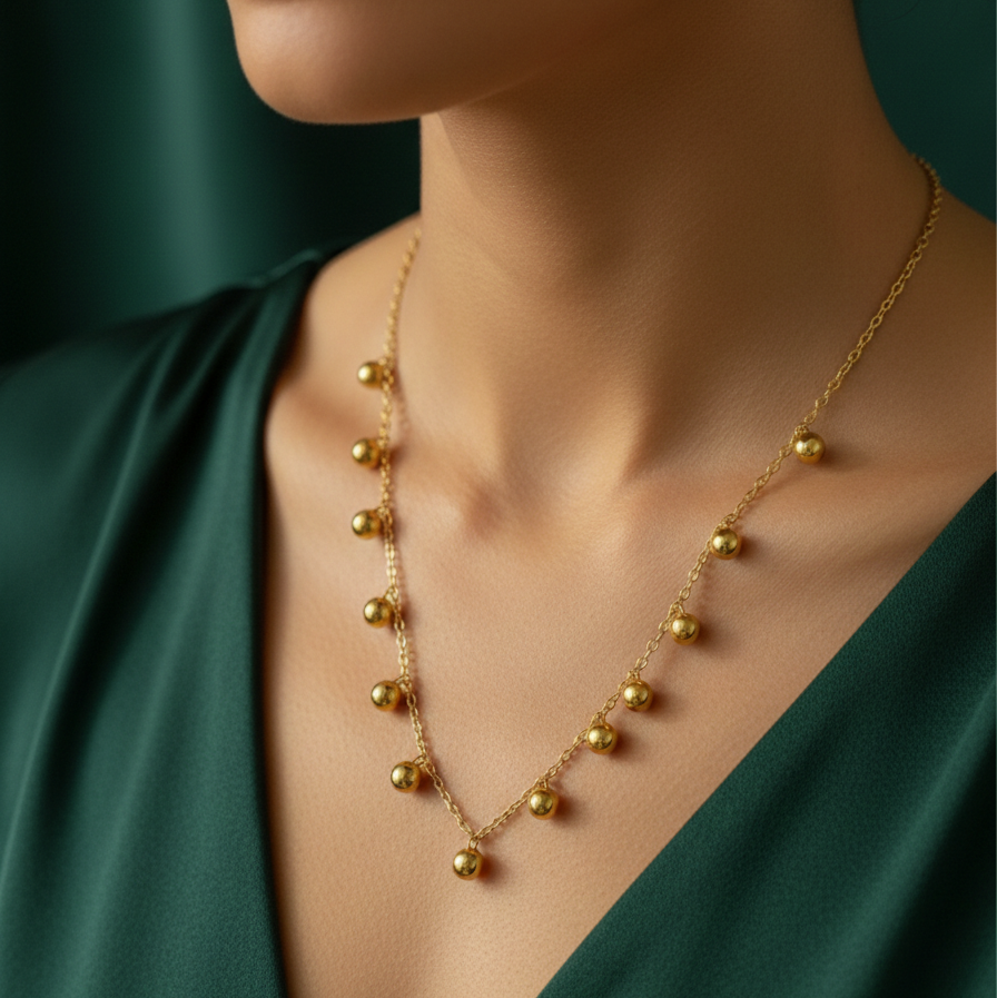 Gold necklace with dangling gold ball charms in wooden jewelry box display.