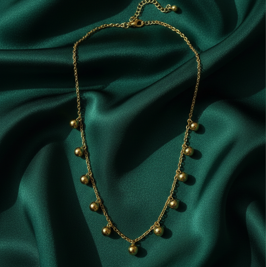 Gold necklace with dangling gold ball charms in wooden jewelry box display.