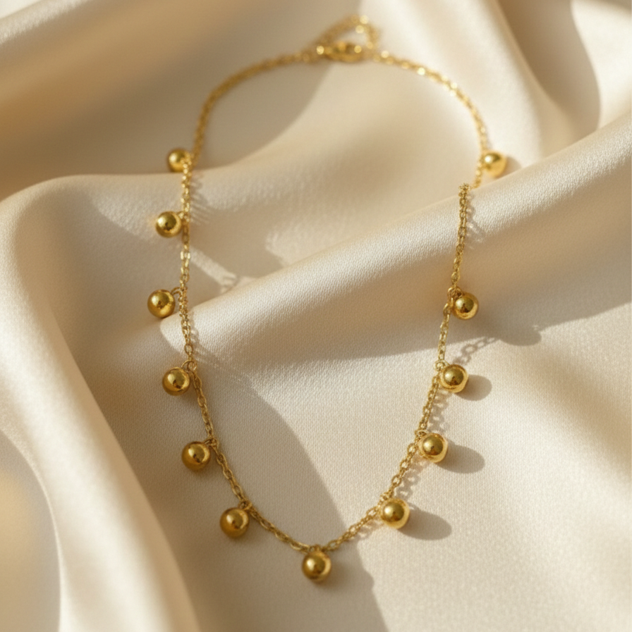 Gold necklace with dangling gold ball charms in wooden jewelry box display.