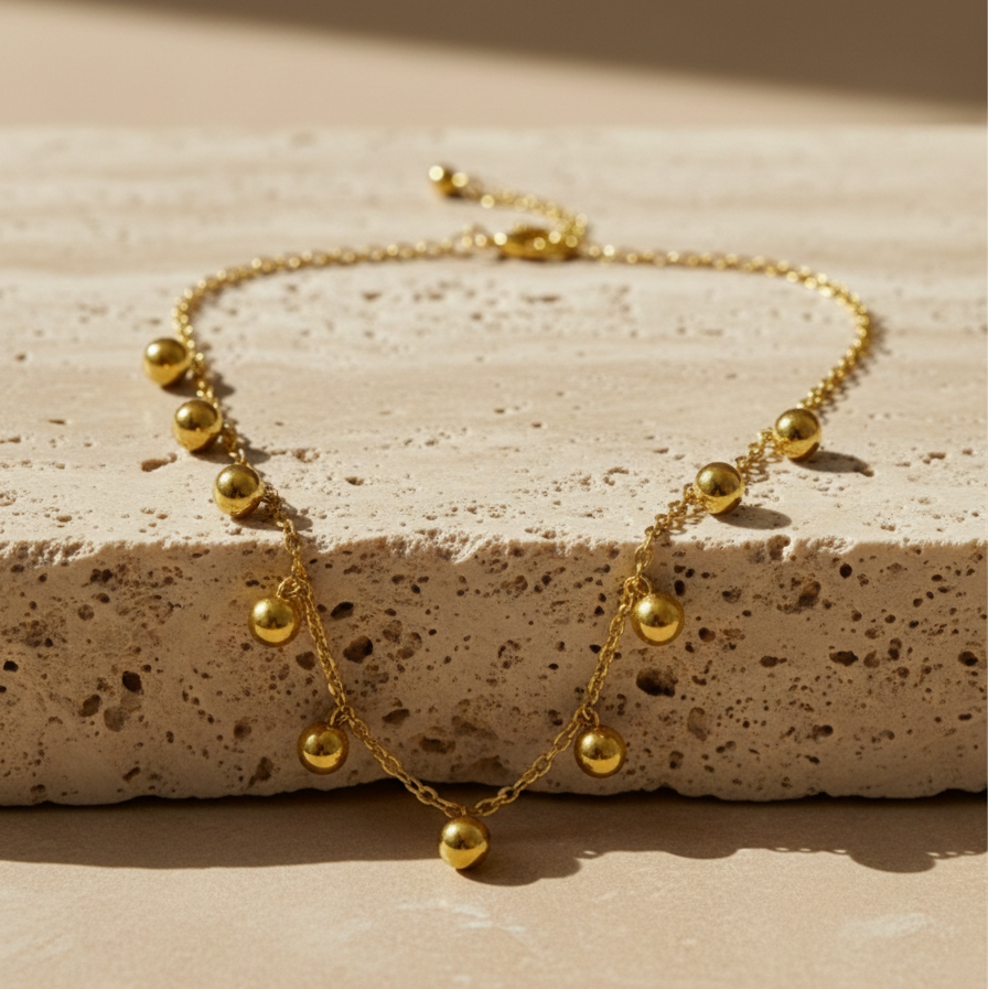 Gold necklace with dangling gold ball charms in wooden jewelry box display.