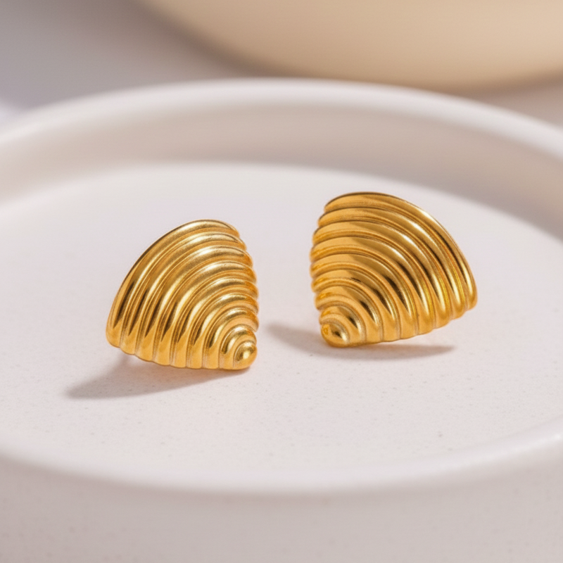 Ribbed gold croissant style triangular stud earrings on white background.
