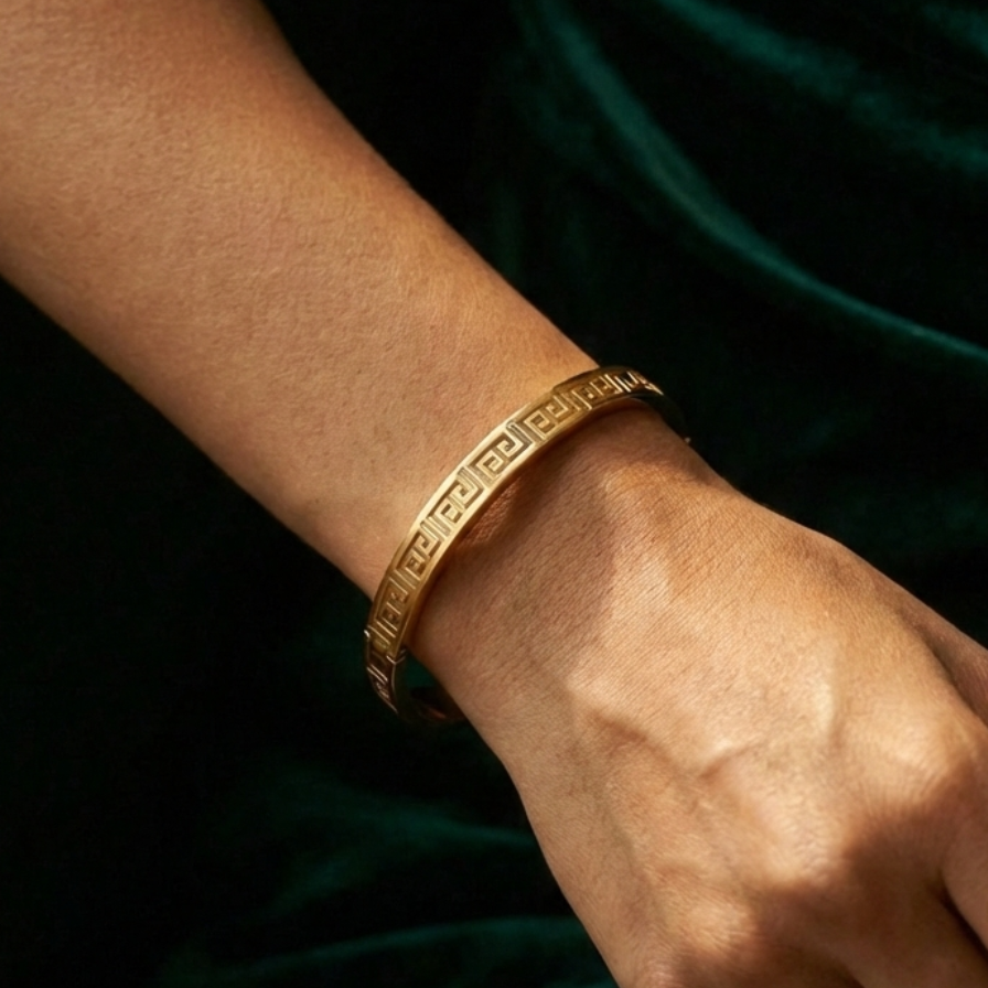 Gold oval bangle bracelet with cut-out Greek Key pattern on white plate.