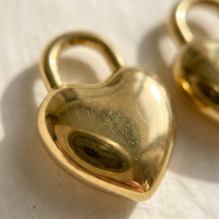 Gold puffy heart padlock earring worn on ear model.