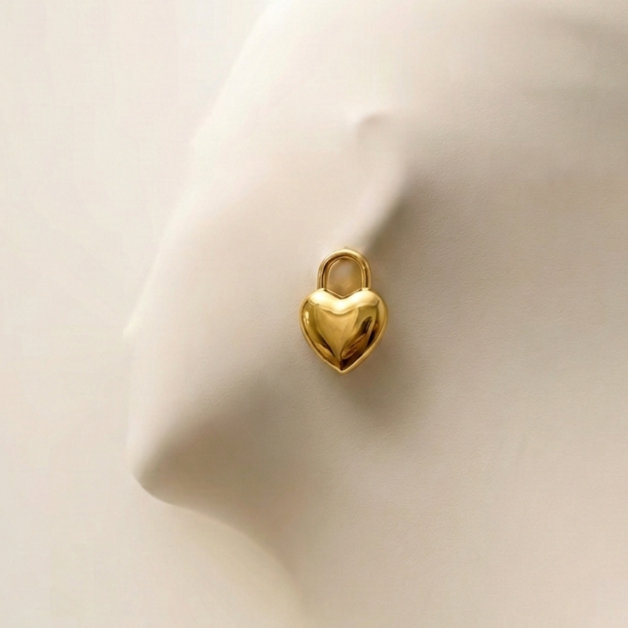 Gold puffy heart padlock earring worn on ear model.