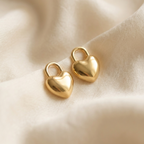 Gold puffy heart padlock earring worn on ear model.