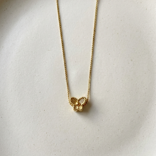 Small gold butterfly pendant with textured wings on white plate.