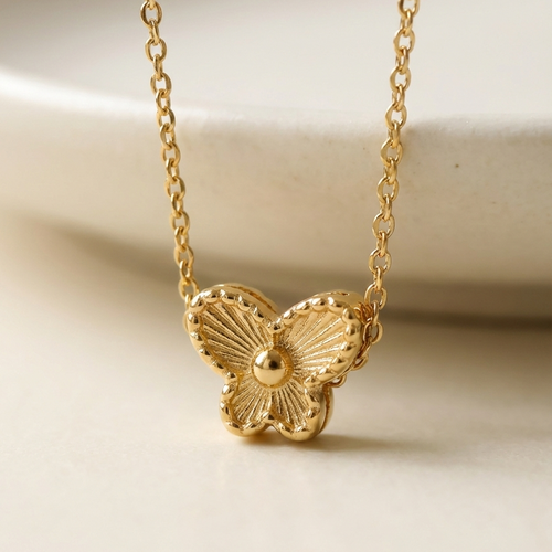 Small gold butterfly pendant with textured wings on white plate.