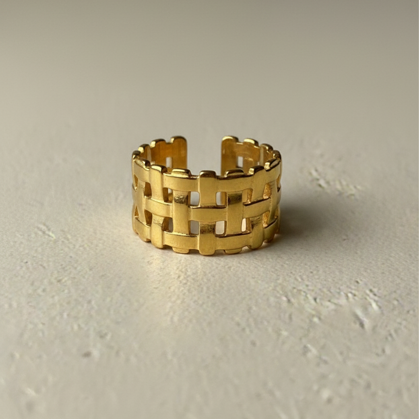 Wide gold ring with woven basket weave texture on white background.