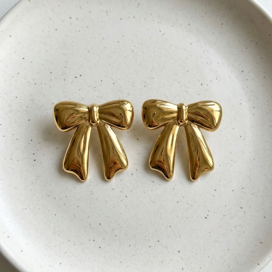 Large gold ribbon bow stud earrings on white background.