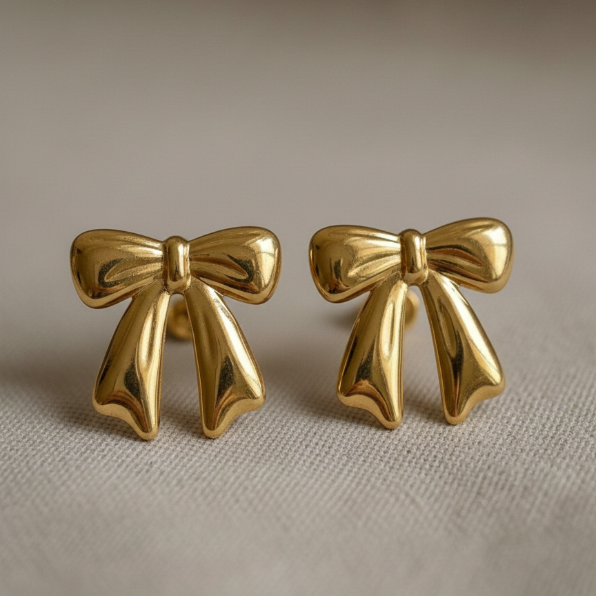 Large gold ribbon bow stud earrings on white background.
