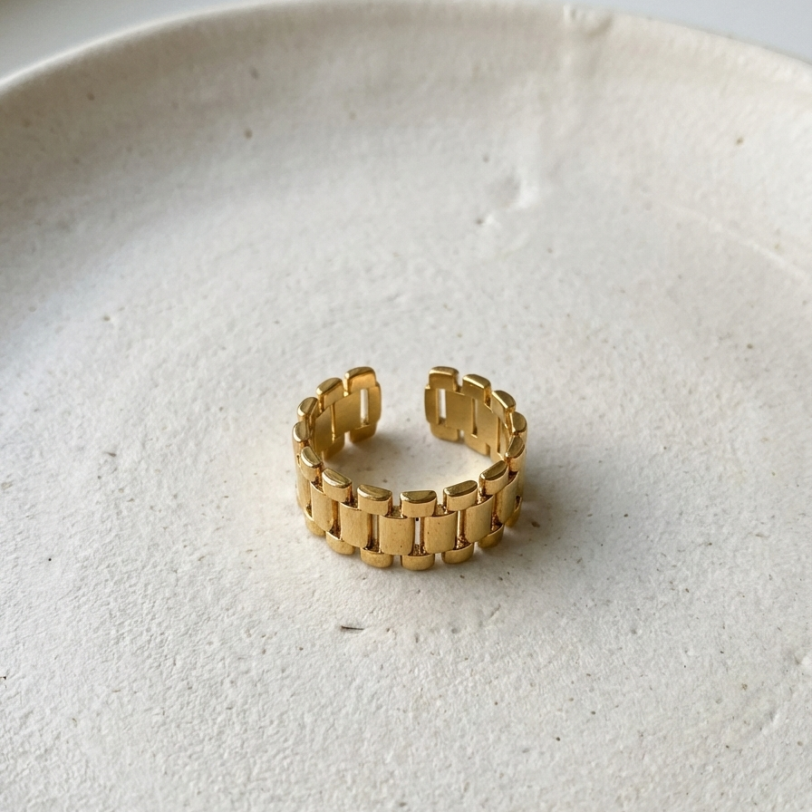 Chunky gold ring with watch strap link design on green silk fabric.