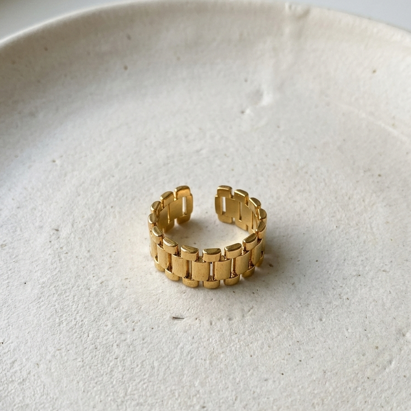 Chunky gold ring with watch strap link design on green silk fabric.