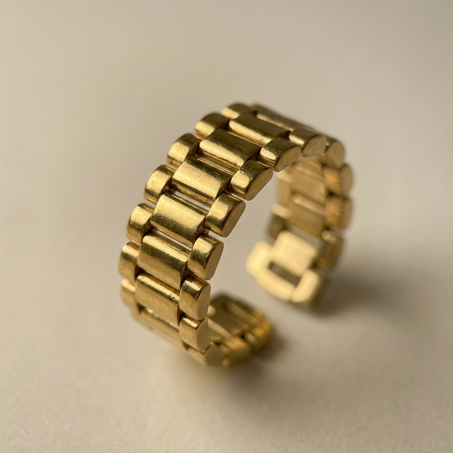Chunky gold ring with watch strap link design on green silk fabric.
