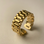 Chunky gold ring with watch strap link design on green silk fabric.