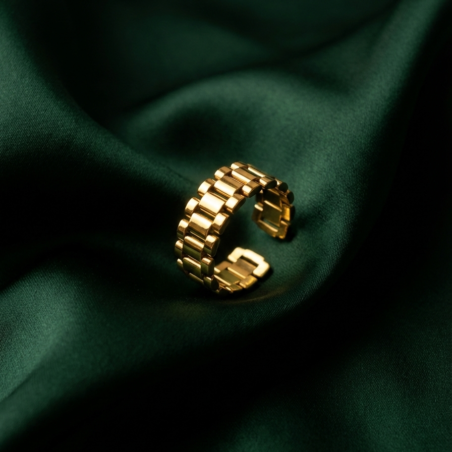 Chunky gold ring with watch strap link design on green silk fabric.