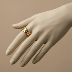 Chunky gold ring with watch strap link design on green silk fabric.