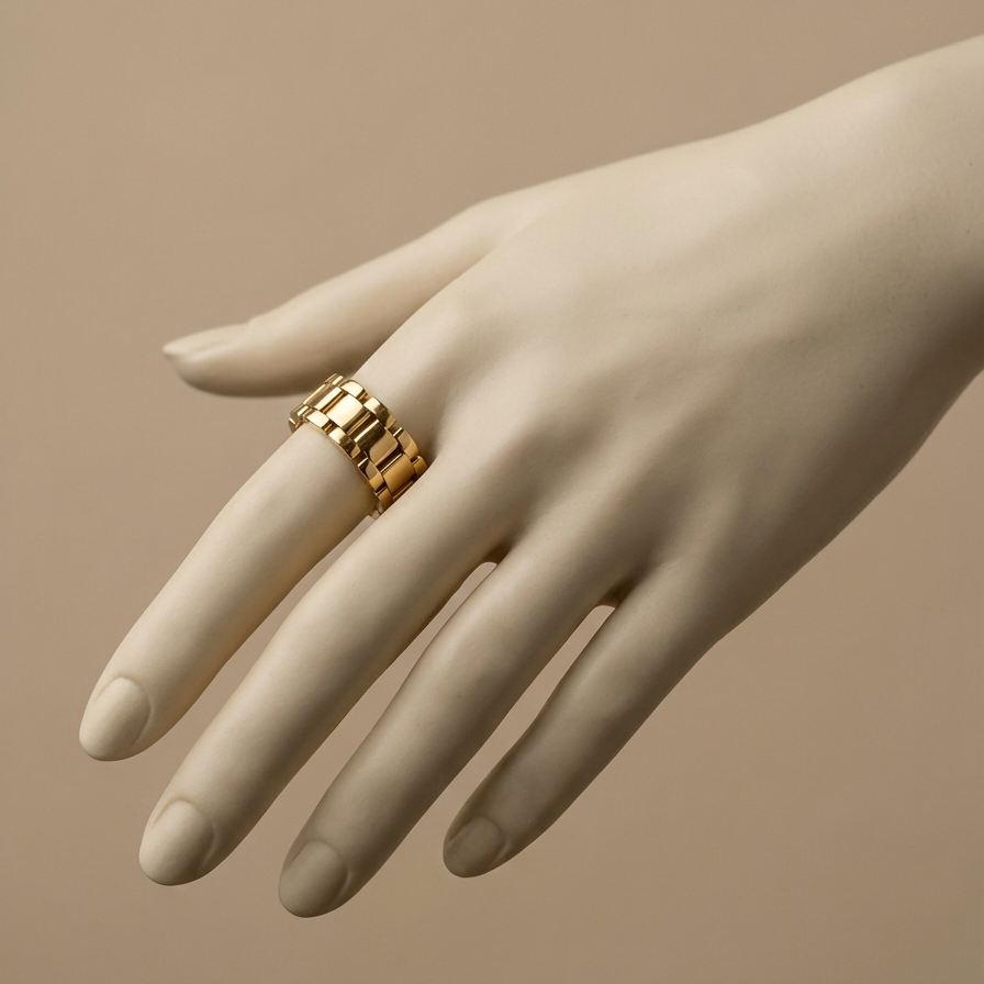 Chunky gold ring with watch strap link design on green silk fabric.