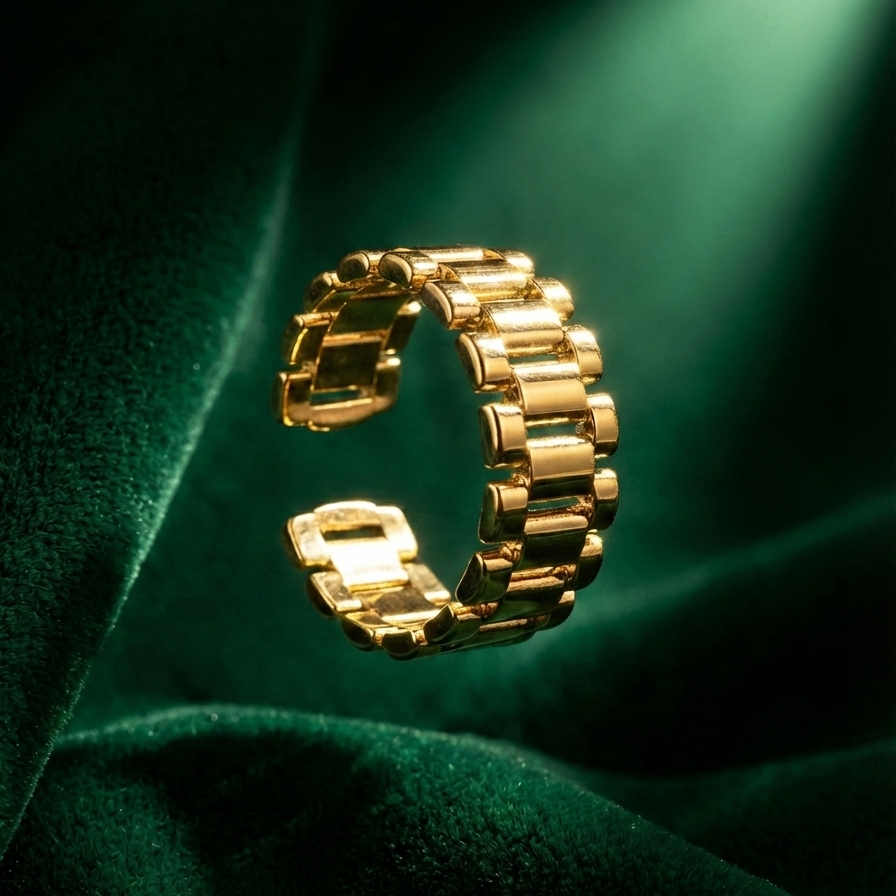 Chunky gold ring with watch strap link design on green silk fabric.