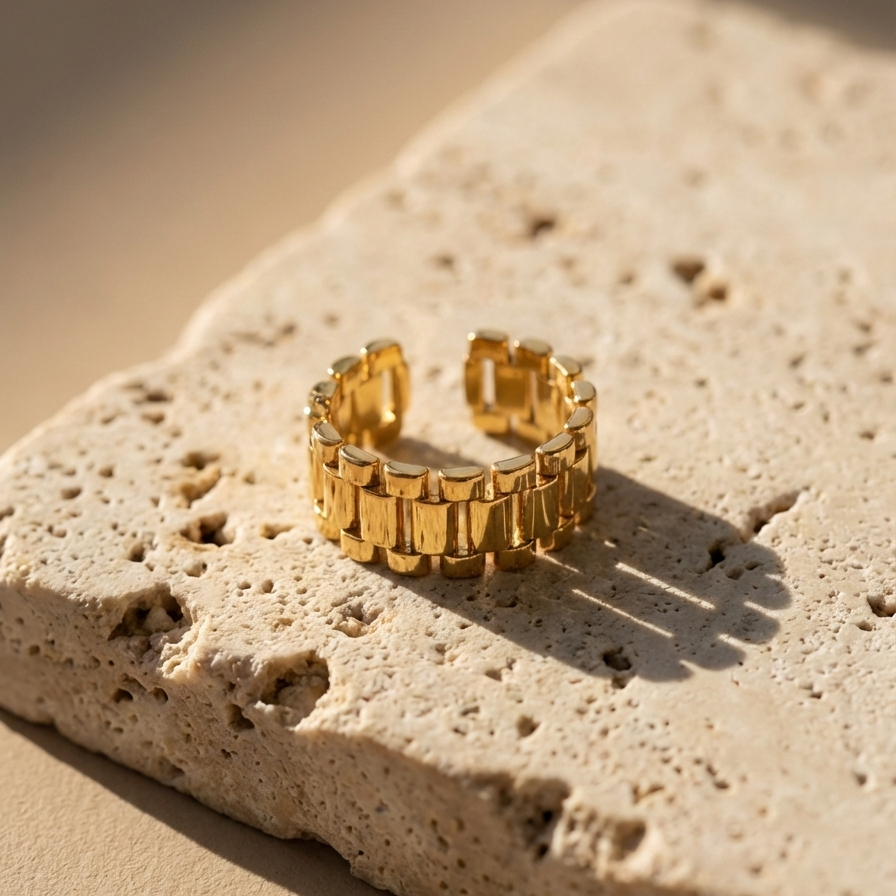 Chunky gold ring with watch strap link design on green silk fabric.