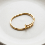 Gold bent nail design bangle bracelet on white stone prop.