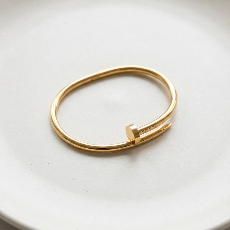 Gold bent nail design bangle bracelet on white stone prop.