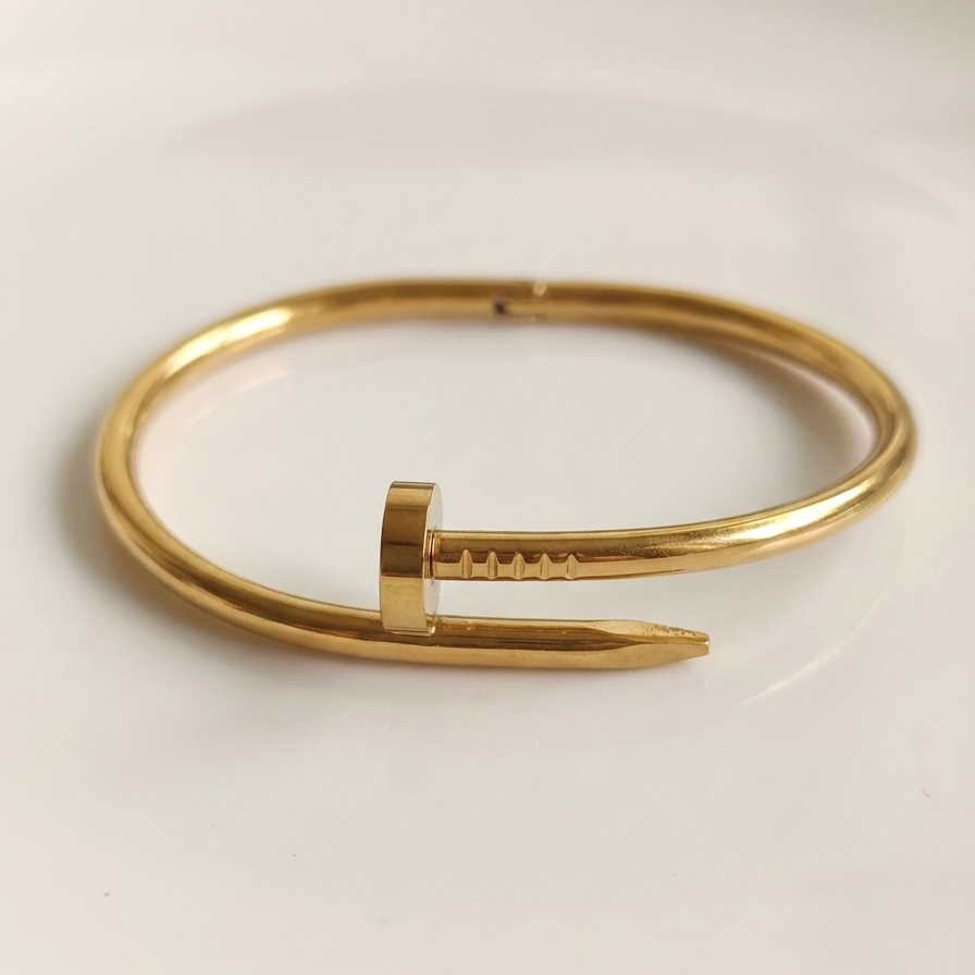 Gold bent nail design bangle bracelet on white stone prop.