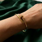 Gold bent nail design bangle bracelet on white stone prop.