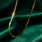 Flat gold herringbone snake chain necklace liquid gold texture waterproof 18k plated on beige silk.