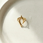 Gold wave ring with open adjustable design on white stone background.