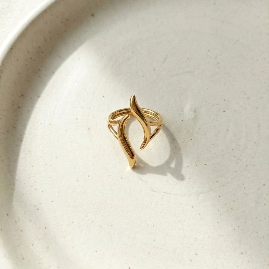 Gold wave ring with open adjustable design on white stone background.