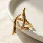 Gold wave ring with open adjustable design on white stone background.