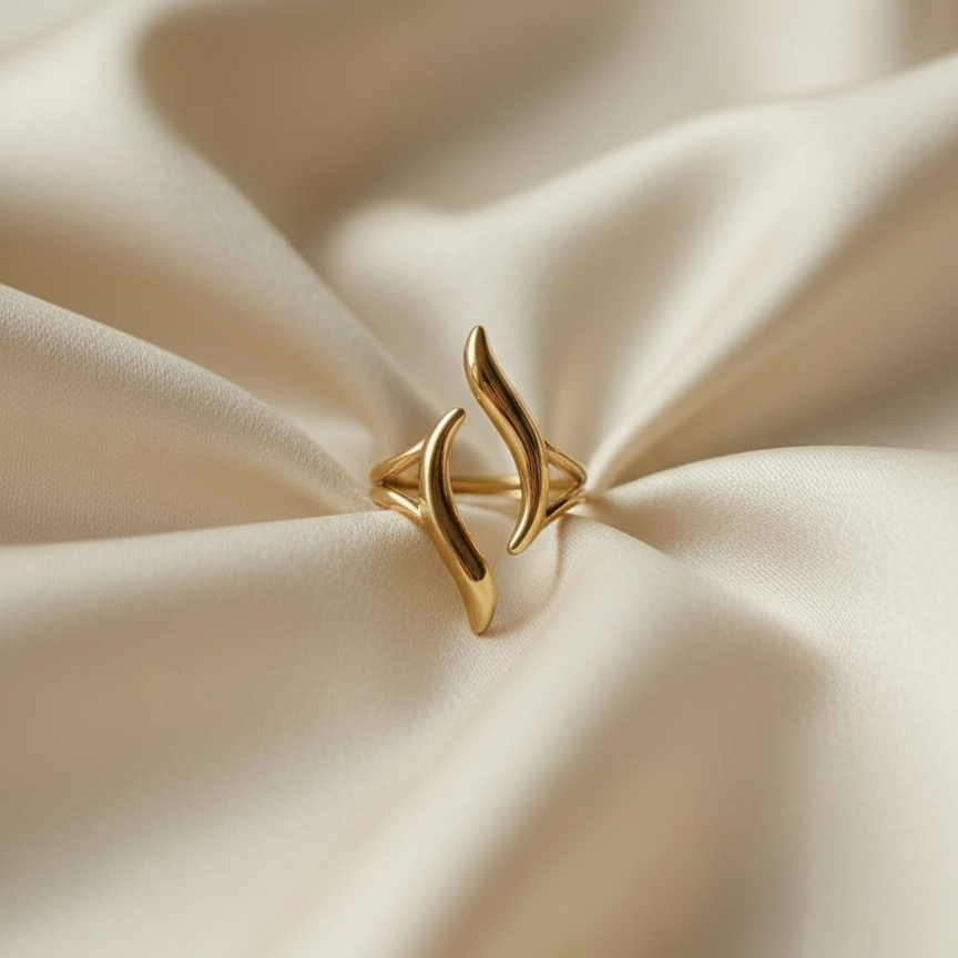 Gold wave ring with open adjustable design on white stone background.