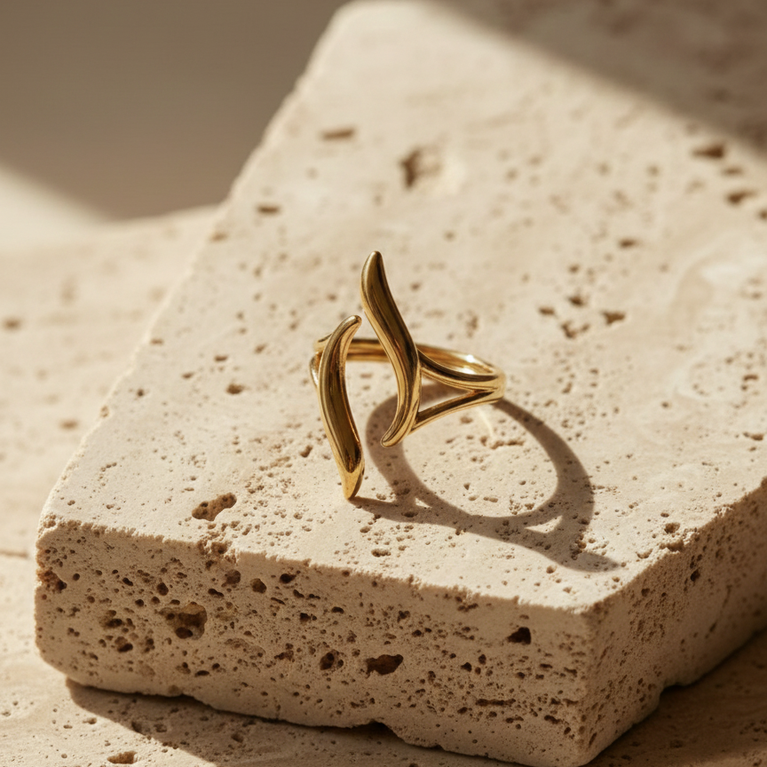 Gold wave ring with open adjustable design on white stone background.