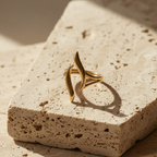 Gold wave ring with open adjustable design on white stone background.