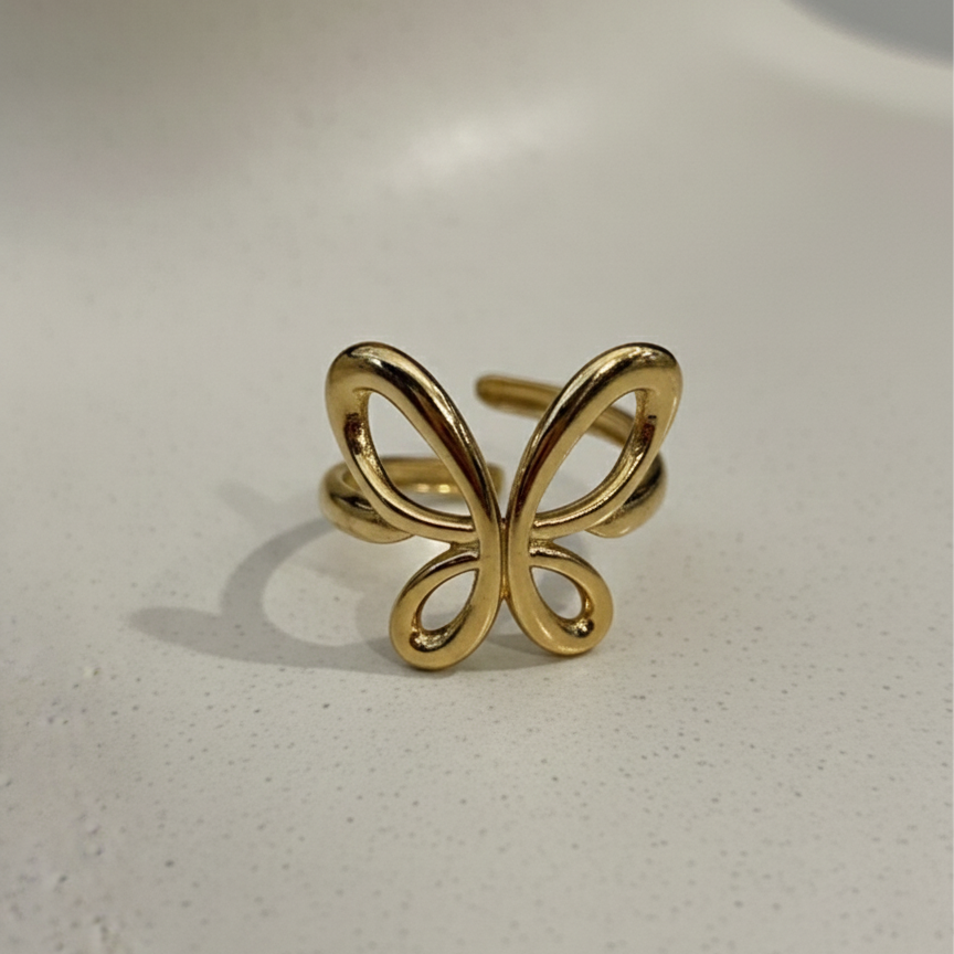 Gold ring with open wire butterfly design standing on white surface.