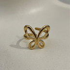 Gold ring with open wire butterfly design standing on white surface.