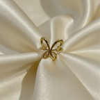 Gold ring with open wire butterfly design standing on white surface.