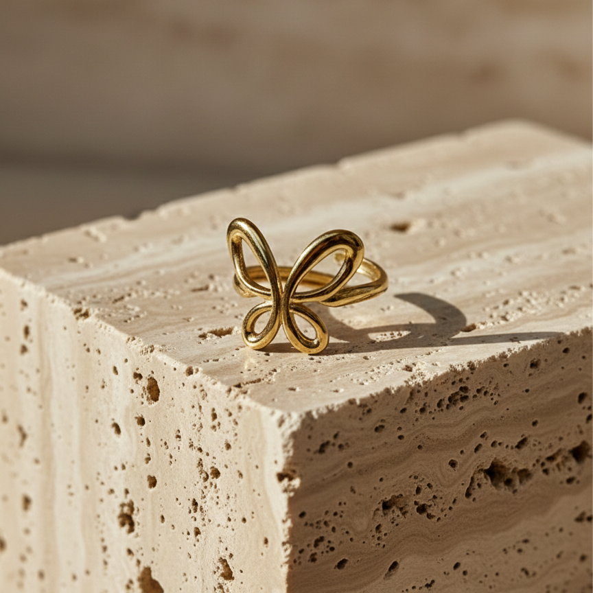 Gold ring with open wire butterfly design standing on white surface.