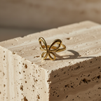 Gold ring with open wire butterfly design standing on white surface.