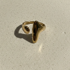 Abstract gold statement ring with elongated molten shape on white background.